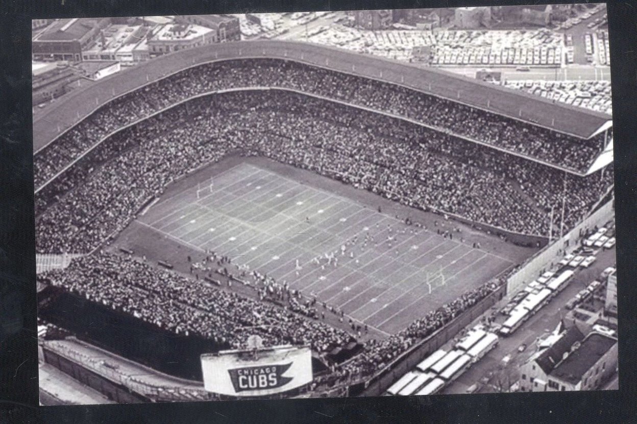 Black-and-white aerial view of a packed Wrigley Field set up for football, with a Chicago Cubs sign and buses outside