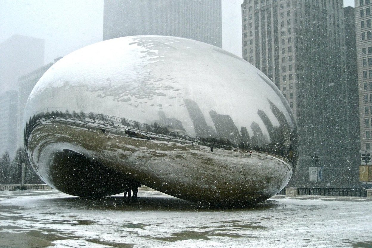 Snow-covered Cloud Gate sculpture reflecting Chicago skyline in winter.