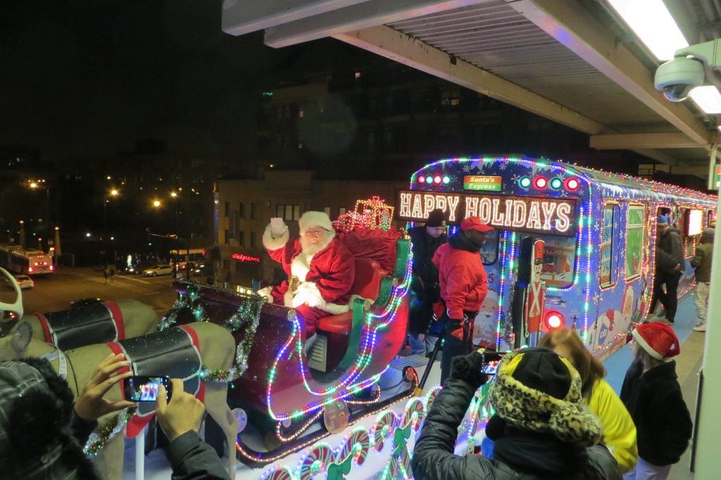 Santa in sleigh on a decorated train with "Happy Holidays" sign.