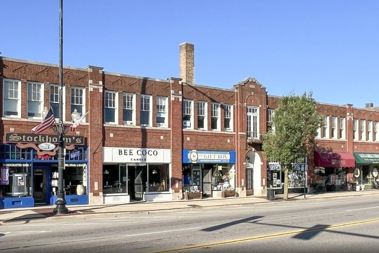 Children in Halloween costumes walking along a downtown Geneva, Illinois sidewalk past storefronts with trick-or-treat signs in the windows.