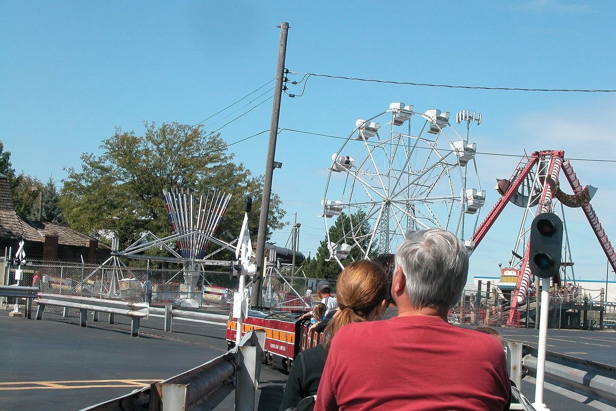 Riders at Kiddieland in Melrose Park with the Ferris wheel and swing ride behind them, 2007