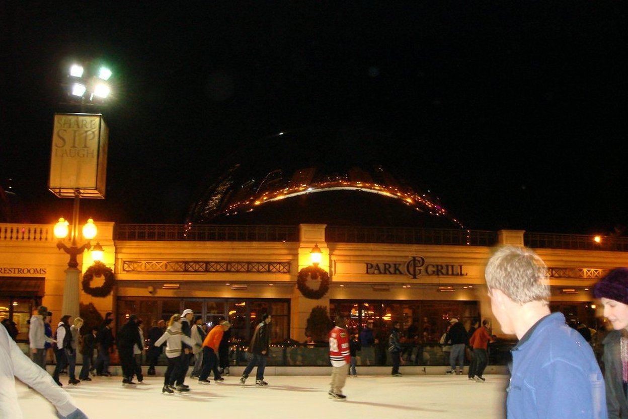 Nighttime ice rink with people skating in front of Park Grill and a lit roller coaster.