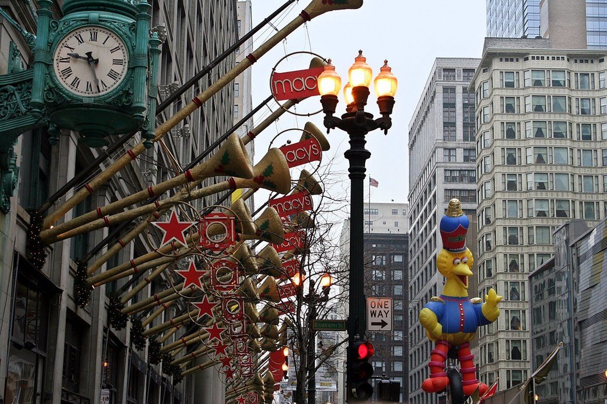 Macy's holiday decorations with giant horns and a parade balloon on a city street.