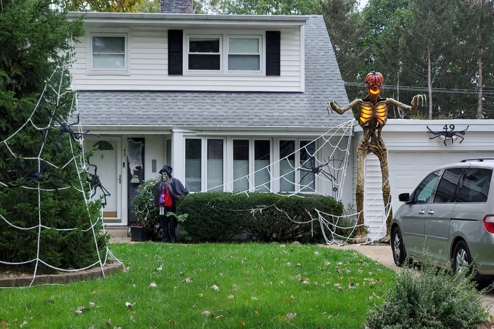 A suburban Chicagoland front yard set up for Halloween with a giant rope spider web and a tall glowing skeleton