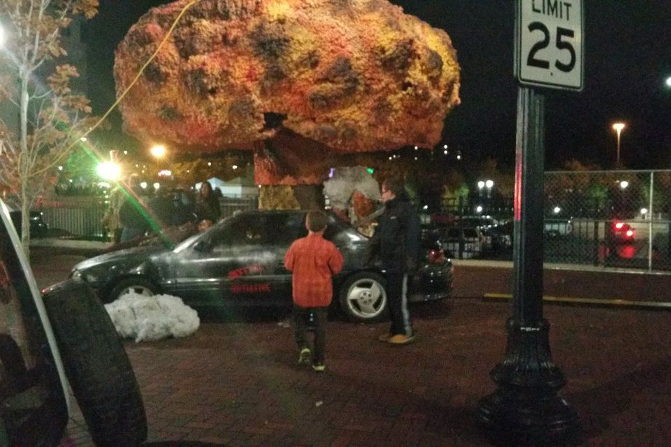 A staged wreck scene with a smashed car and a huge glowing prop on a downtown Elgin street during Nightmare on Chicago Street, 2015